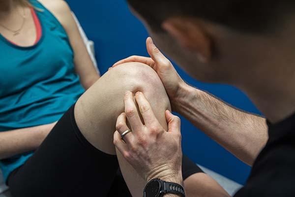 Close-up of a man asessing someone's knee while the person is sat on a treatment bench.